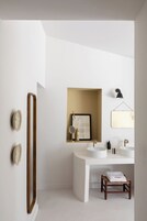 Un baño moderno con un espejo grande, dos lavamanos, un cuadro enmarcado y un taburete pequeño de madera.
