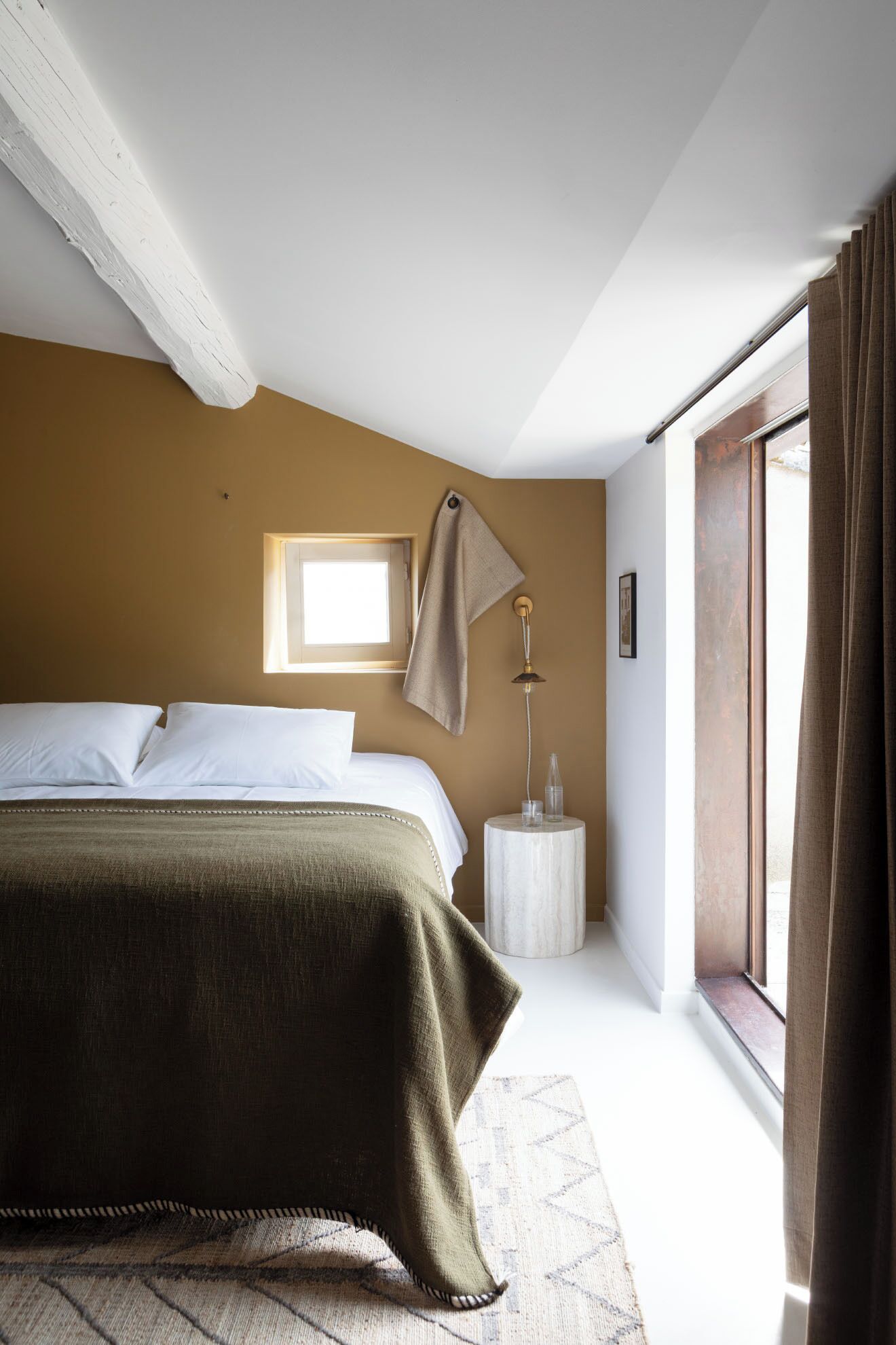 Un dormitorio con cama, mesita de noche, lámpara, ventana y vistas al exterior.