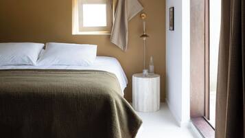 Un dormitorio con cama, mesita de noche, lámpara, ventana y vistas al exterior.