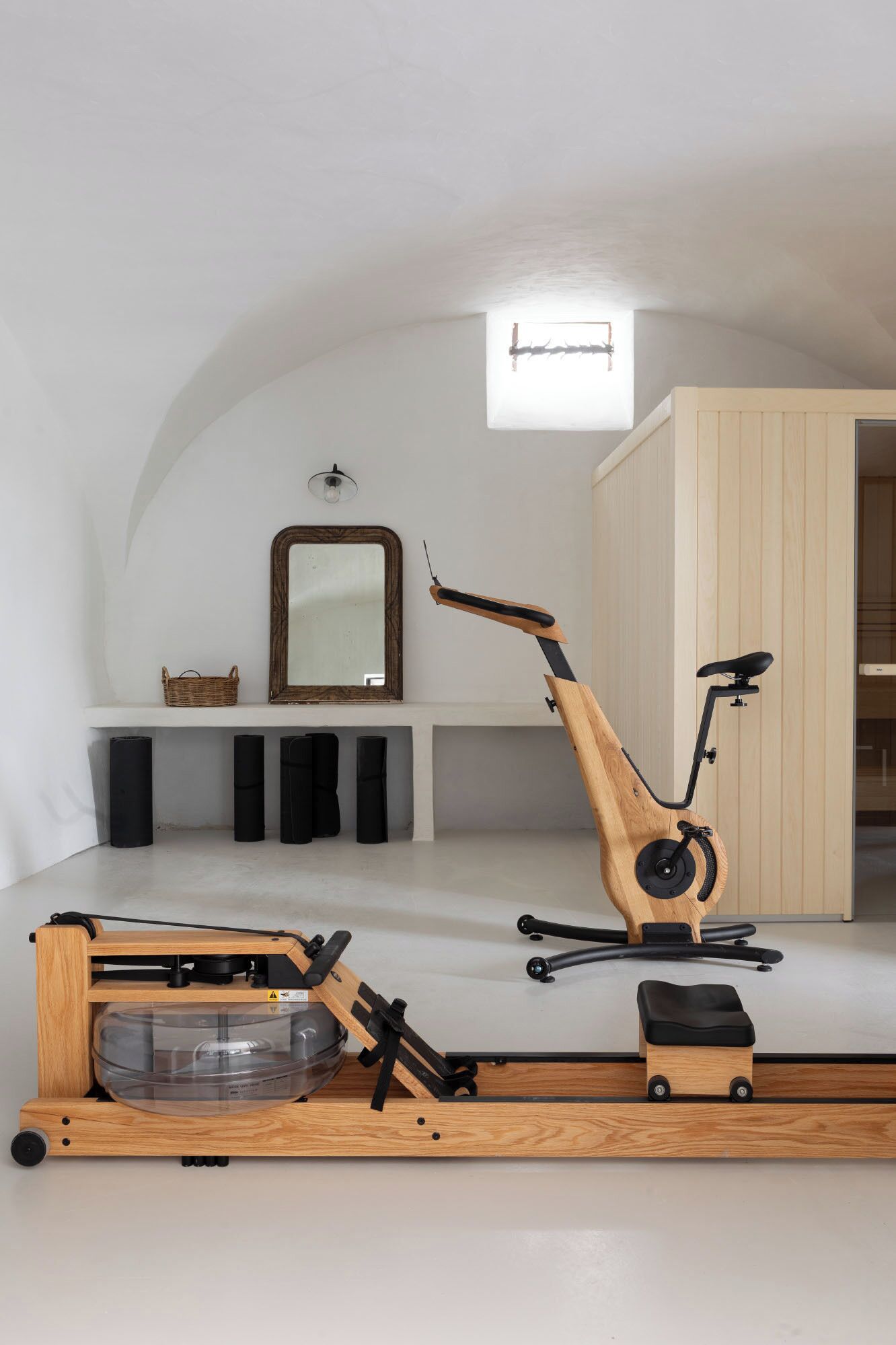 Une pièce de taille modeste, dotée d’un ventilateur de plafond, d’un miroir, d’un vélo d’exercice en bois et d’un petit tabouret.