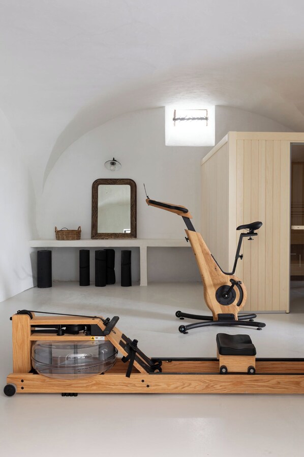 Habitación compacta con ventilador de techo, espejo, bicicleta estática de madera y un taburete pequeño.