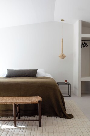 A bedroom with a bed, a bench, a hanging light, a nightstand, and a wardrobe.