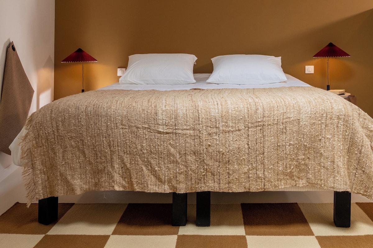 A bedroom with a bed, two bedside lamps, a window, and a checkered floor.