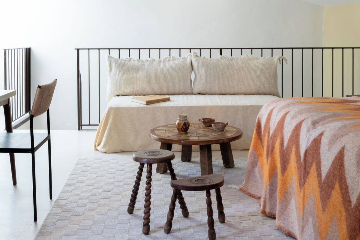 A bedroom with a bed, bedside tables, a hanging light fixture, and a view of the sky.