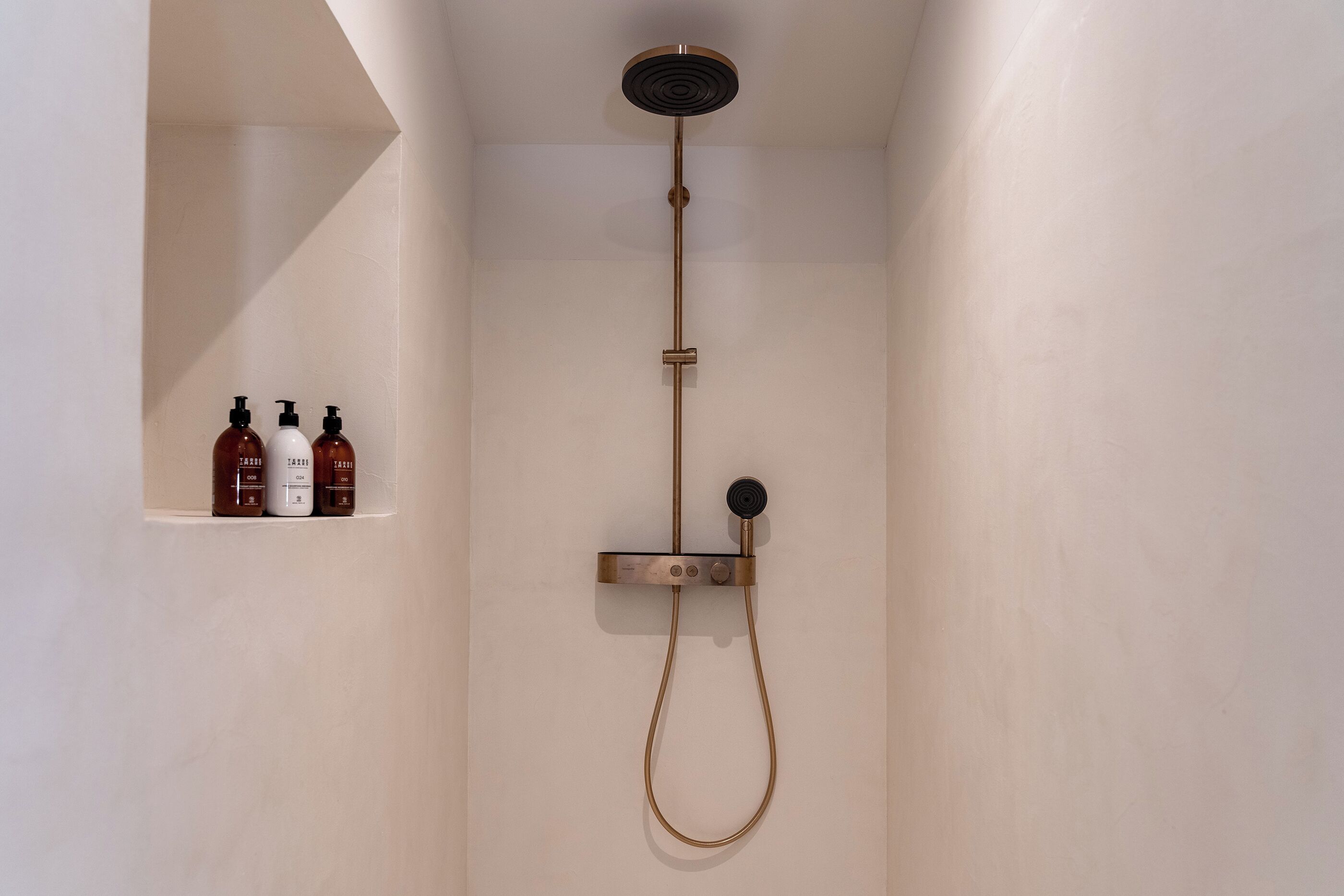 Un área de ducha minimalista con un cabezal de ducha de mano y un panel de control en la pared.