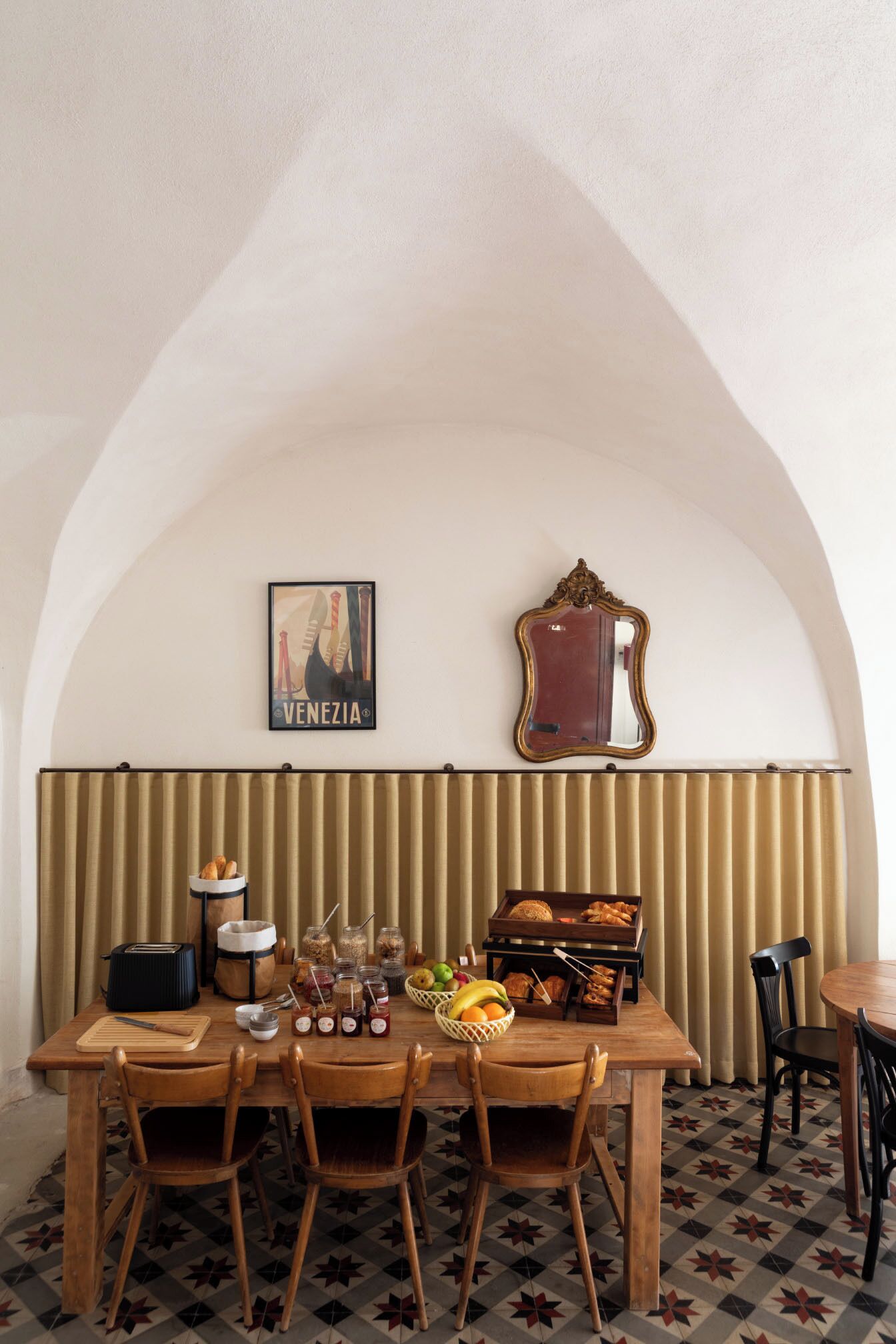 A dining area with a wooden table set for four, a vintage mirror, and a framed poster on the wall.