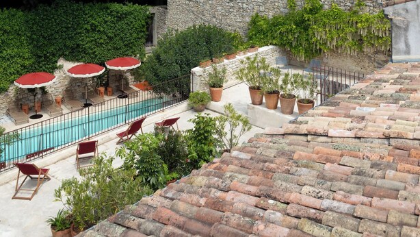 Un espace piscine aménagé sur le toit, avec des murs en pierre, des plantes en pot et des sièges d’extérieur.