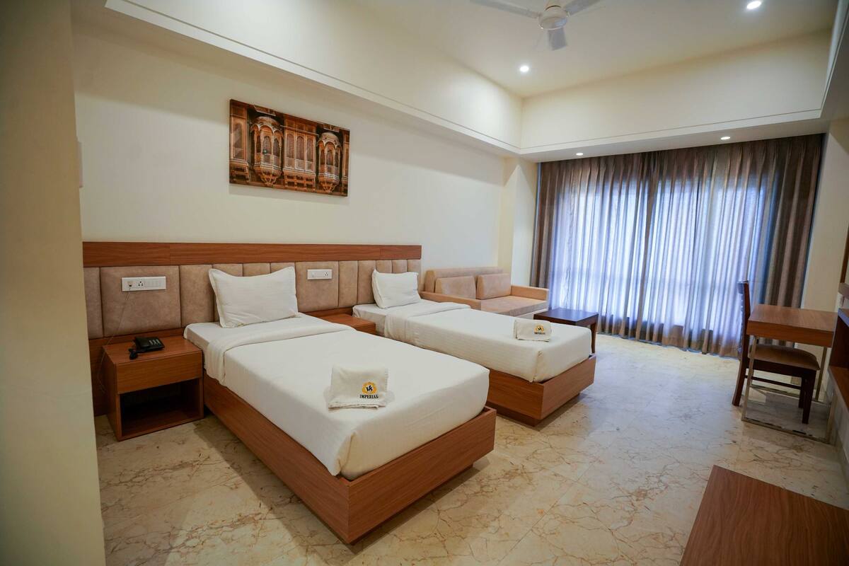 Habitación de hotel con dos camas, un escritorio, una silla y un ventanal con cortinas.