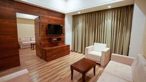 A modern living room with a wooden floor, a flat-screen TV, a wooden cabinet, a coffee table, and two white sofas. - VS Imperial (Akola)