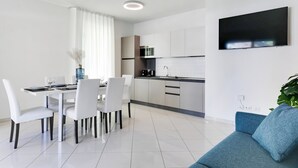 A modern kitchen with white cabinets, a built-in microwave, and a flat-screen TV mounted on the wall. - Residenza Acquamarina - Siroli Collection (Cervia)