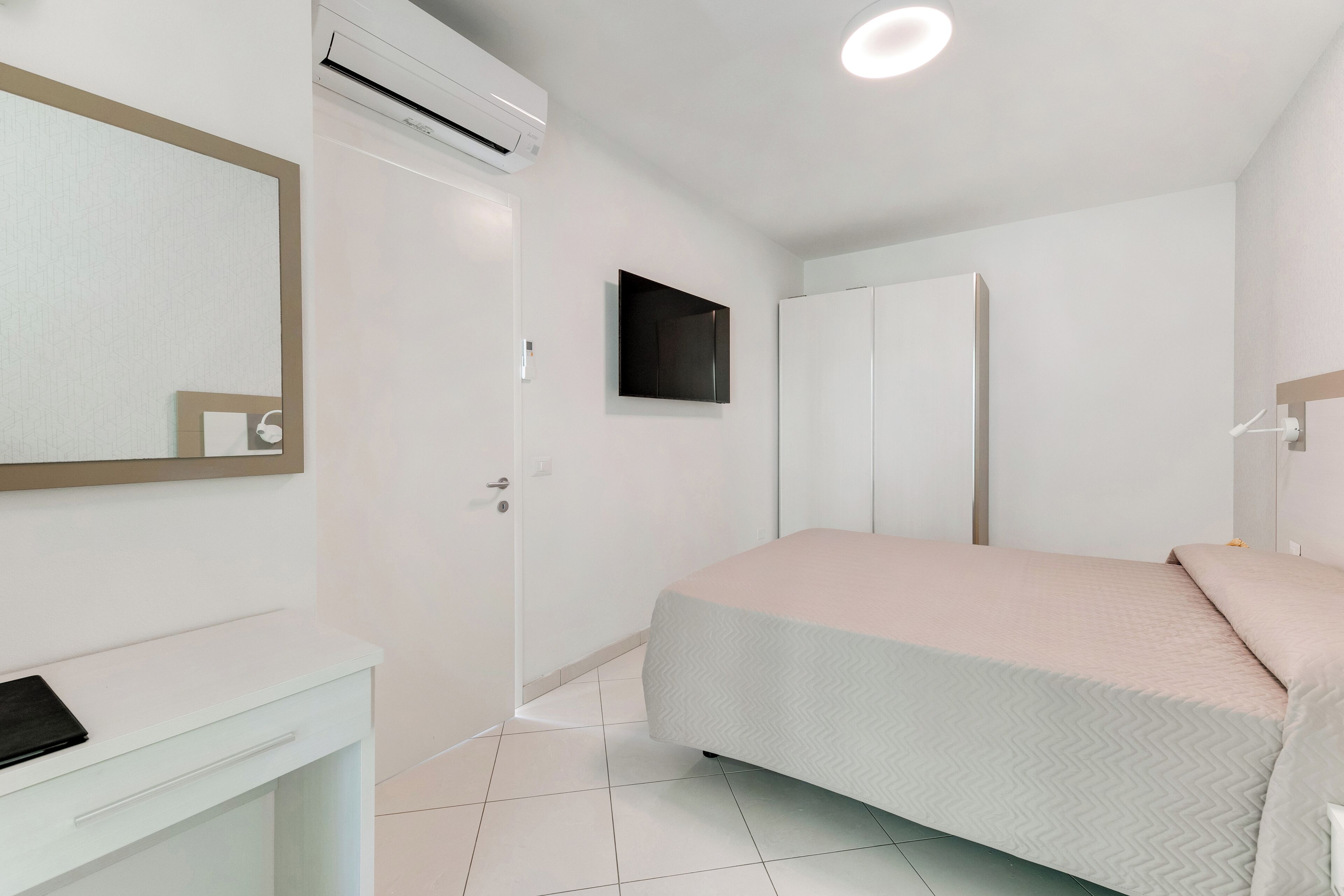 A bedroom with a bed, a wardrobe, a mirror, and an air conditioning unit.