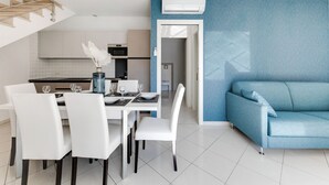 A modern kitchen with white cabinets, a dining table set for four, and a blue accent wall. - Residenza Acquamarina - Siroli Collection (Cervia)