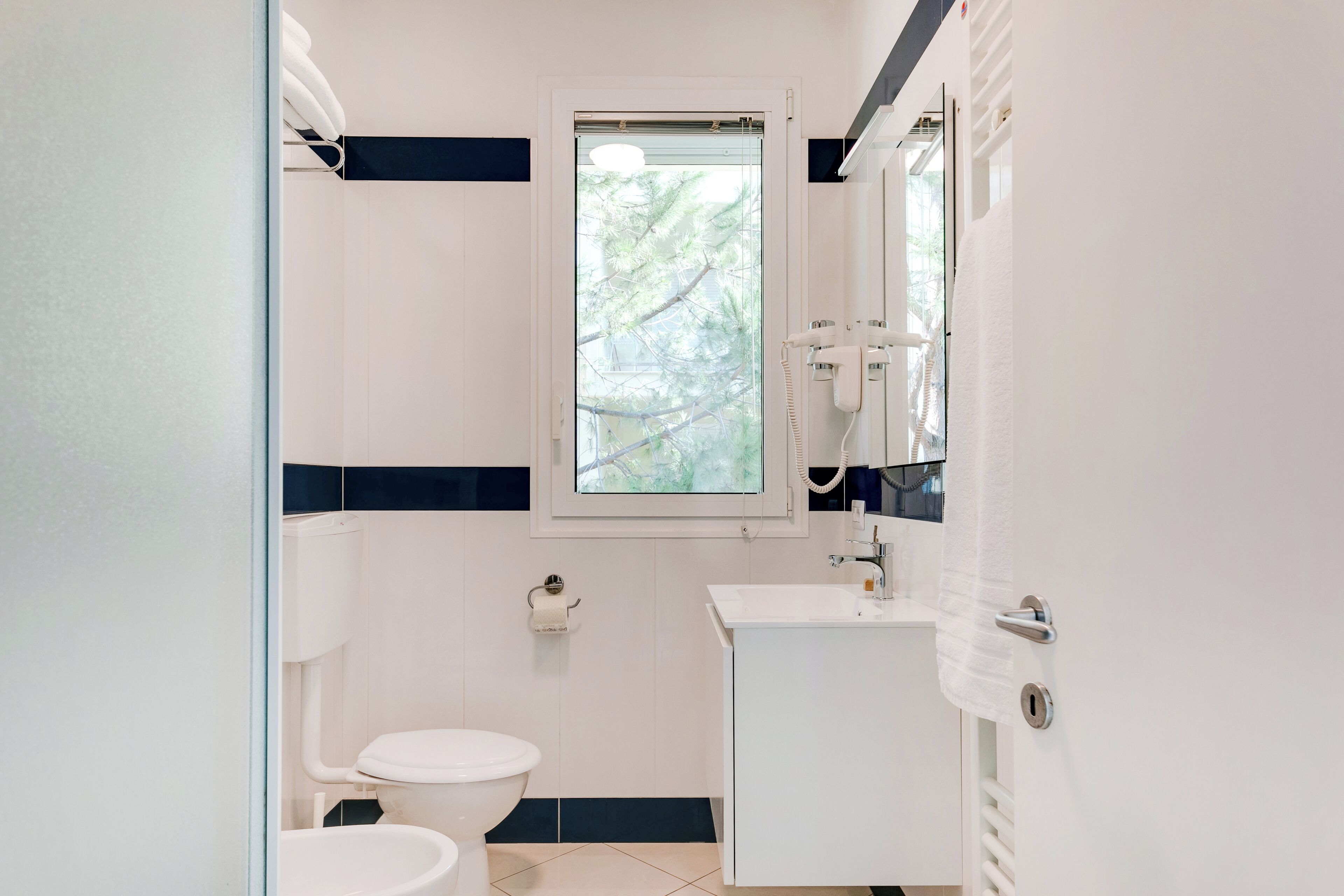Ein Badezimmer mit Toilette, Waschbecken und einem Fenster mit Blick auf Bäume.