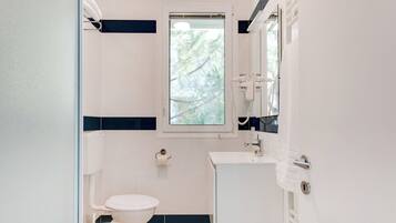 Ein Badezimmer mit Toilette, Waschbecken und einem Fenster mit Blick auf Bäume.