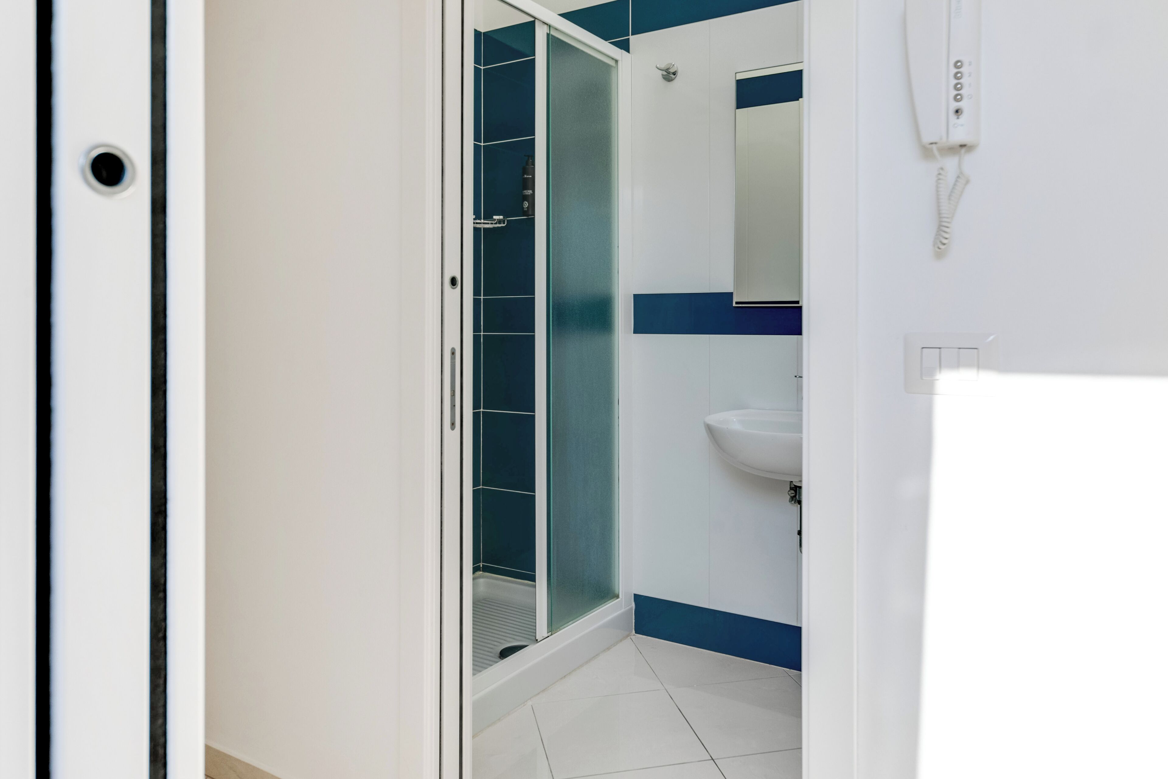 Une salle de bain avec une douche à parois de verre, un lavabo blanc et un téléphone fixé au mur.