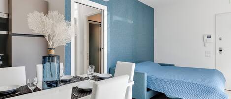 Una habitación de hotel moderna con comedor, una cama con colcha azul y un equipo de aire acondicionado en la pared.