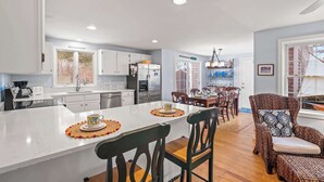 Une cuisine moderne avec des meubles blancs, un grand îlot central et un coin repas doté de chaises en bois.