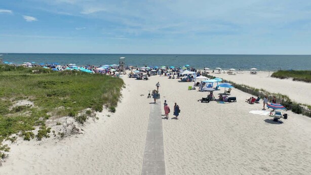 Une plage avec une promenade en bois qui mène à l’eau, bordée de parasols et fréquentée par de nombreux baigneurs.