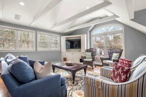 A spacious living room with a high ceiling, large windows, and a cozy seating area with a television and wicker furniture. - Luxury Waterfront with Game Room! (Chatham)
