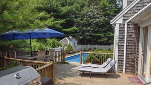 Une terrasse en bois avec un barbecue, des chaises longues et une piscine.