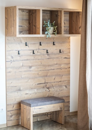Un banco de madera con asiento acolchado y respaldo, ubicado frente a una pared de madera con varios ganchos.