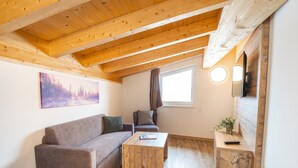 A cozy room with a wooden ceiling, a sofa, a coffee table, and a TV mounted on the wall. - Apartment 50 m From Obingleitn ski Lift (Fieberbrunn)