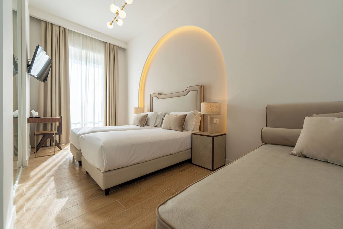 A modern hotel room with a large bed, a smaller bed, a desk, and a TV.