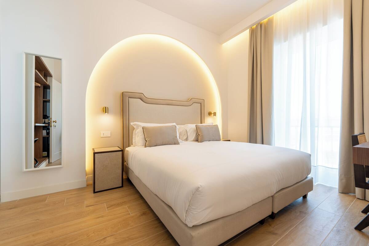 A modern bedroom with a large bed, a bedside table, a mirror, and a wardrobe.
