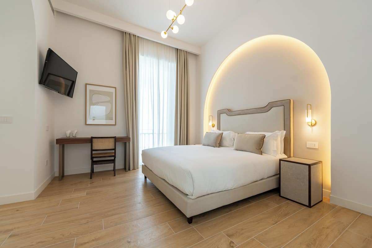 A modern hotel room with a large bed, a desk, and a TV mounted on the wall.