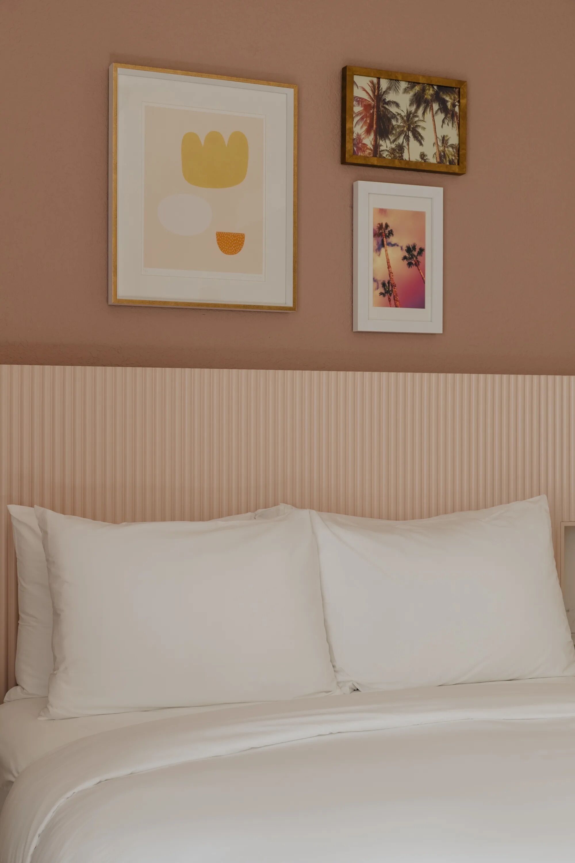 A neatly made bed with white linens in a room with a striped headboard. There are two framed pictures on the wall above the bed.