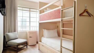 Una habitación con literas, una silla, un refrigerador rosa pequeño y una ventana con cortinas.