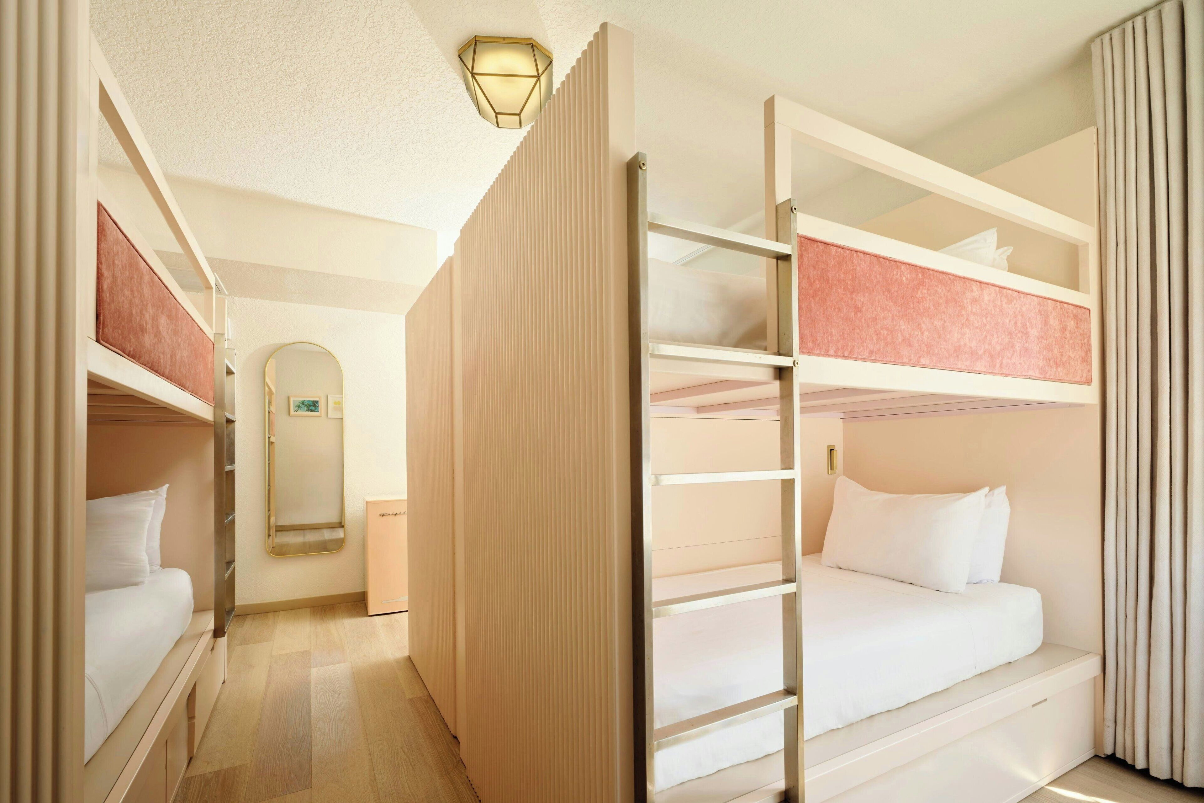 Una habitación de hotel con literas, una mesita de noche, un espejo y una lámpara.
