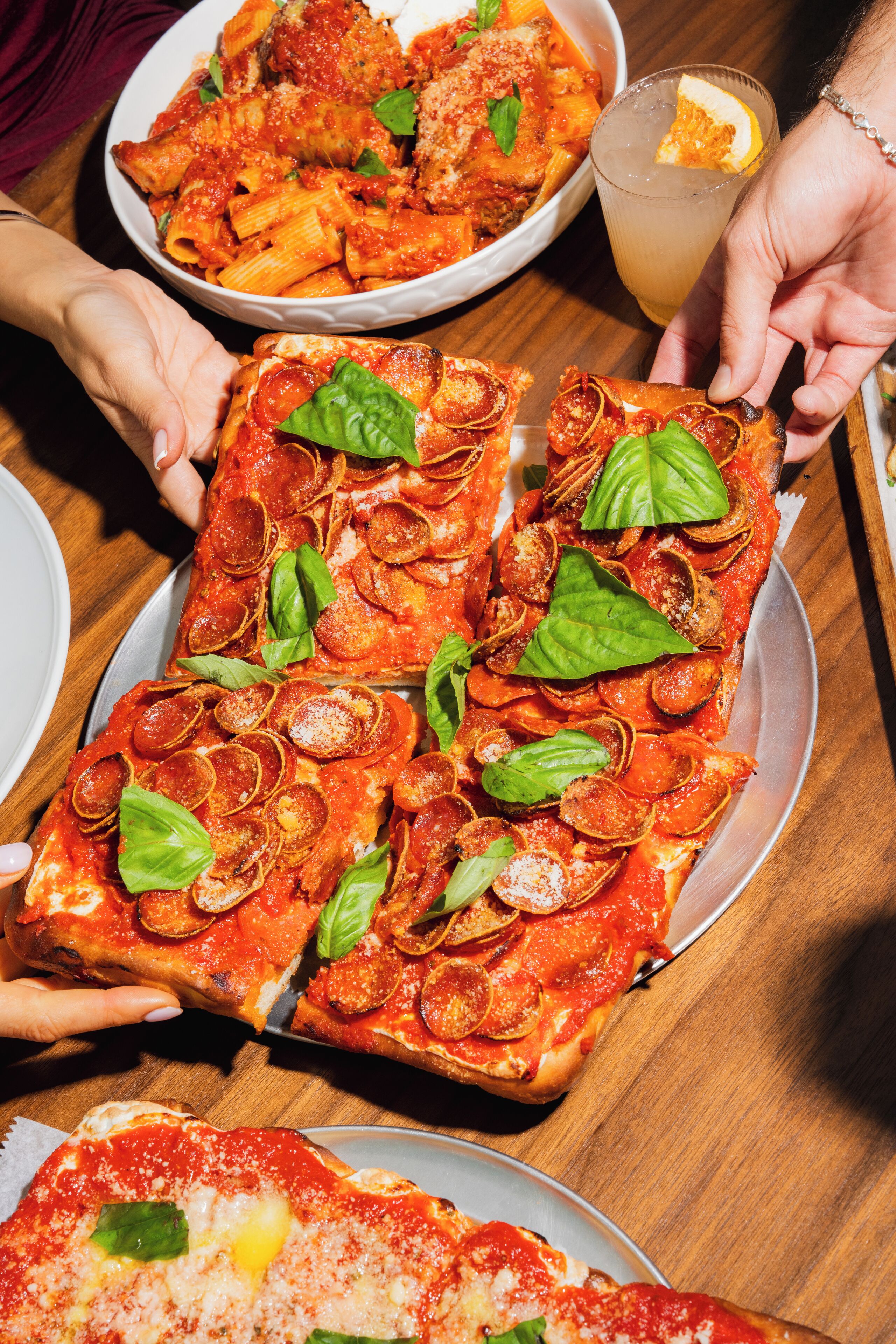 A rectangular pizza with pepperoni and basil on a wooden table.