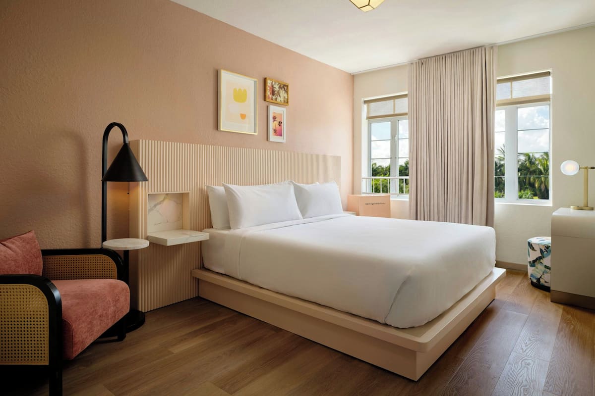Una camera d'albergo moderna con un letto grande, un comodino, una lampada, una sedia e una finestra con tende.
