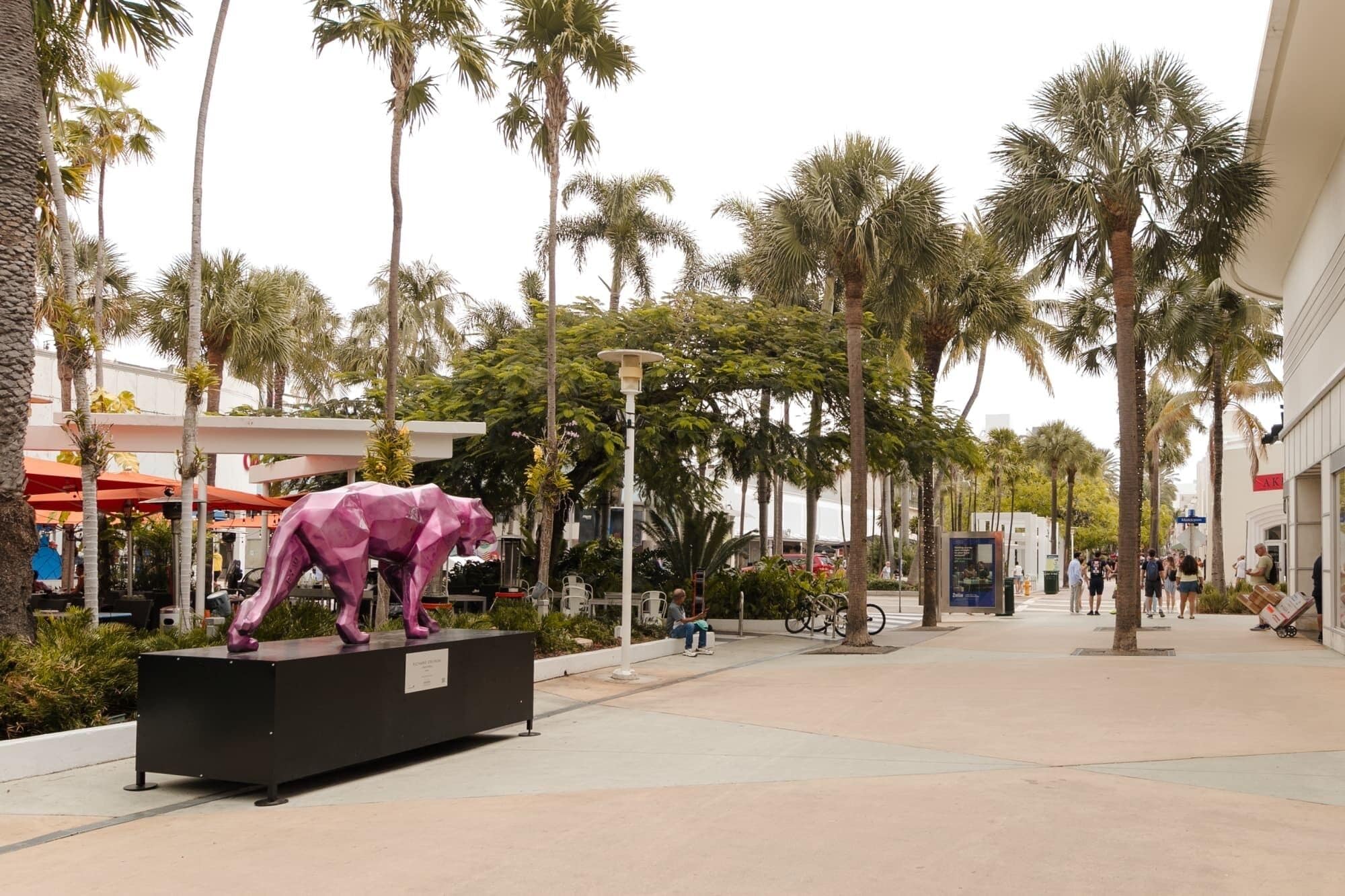A pedestrian walkway lined with palm trees and a large pink sculpture.