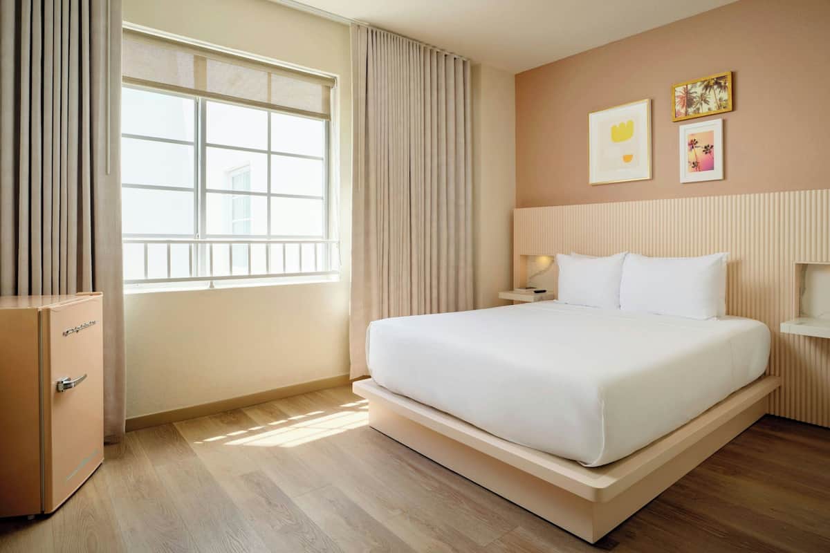 Camera d'albergo con un letto grande, un comodino, una lampada, un armadio e una finestra con tende.