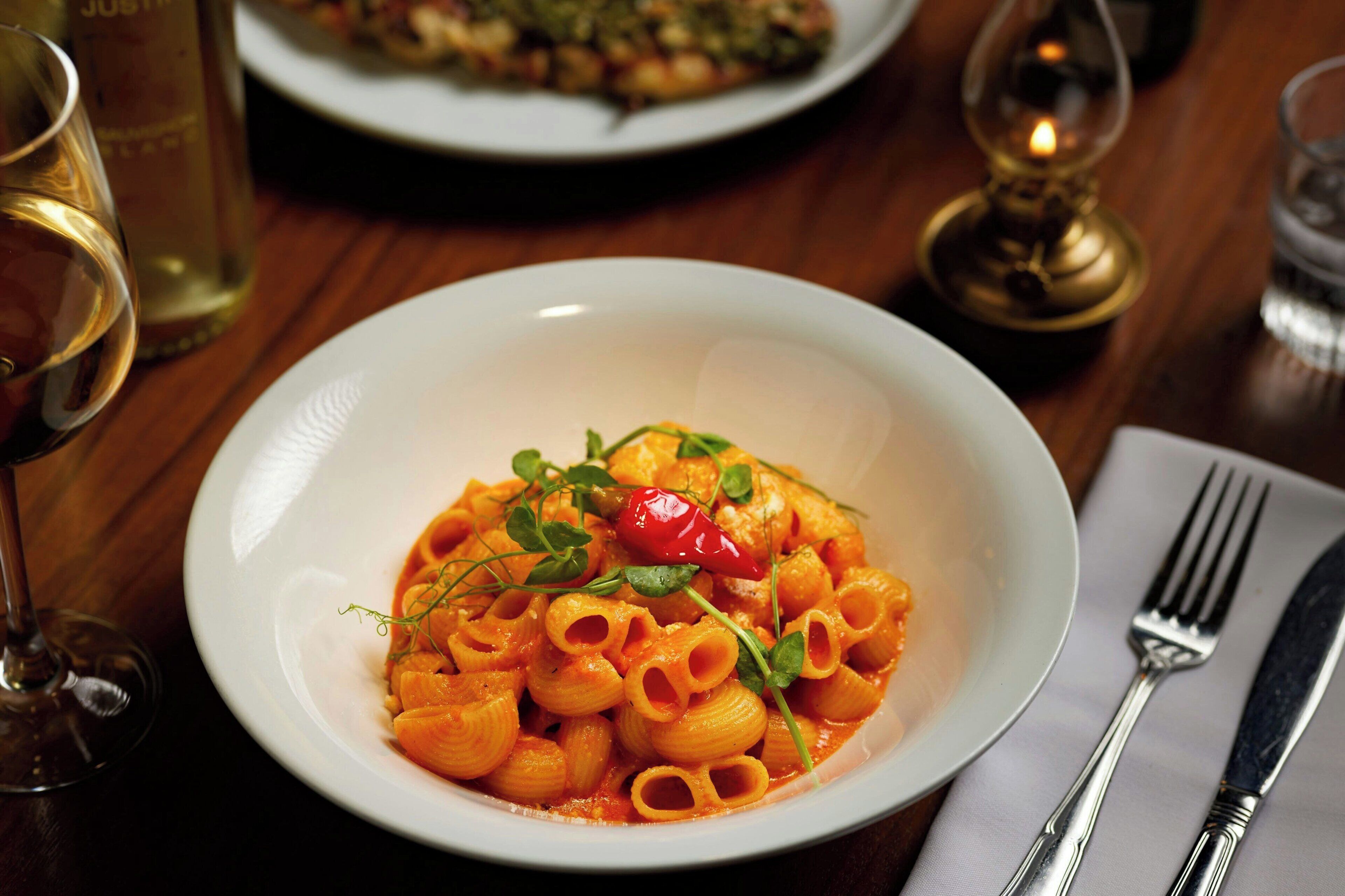 A bowl of pasta with a red chili and greens on a white plate.