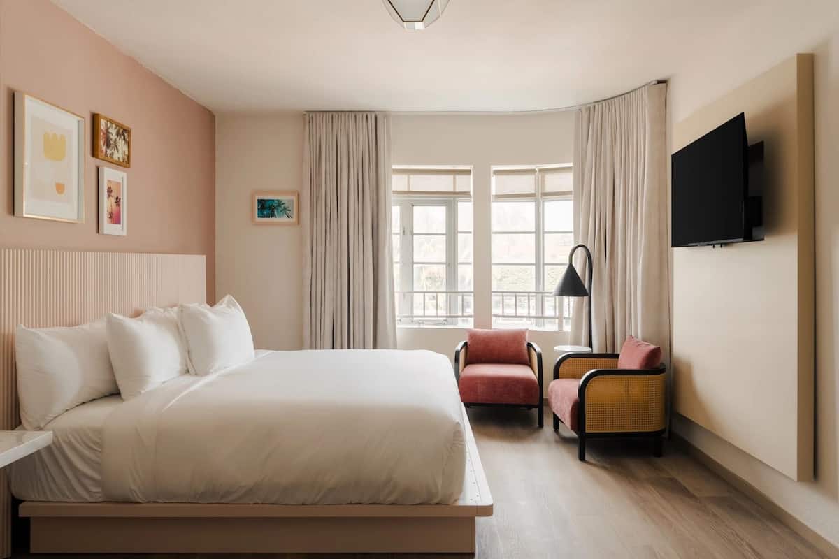 Una camera da letto con un letto, una sedia, una TV e una finestra con tende.