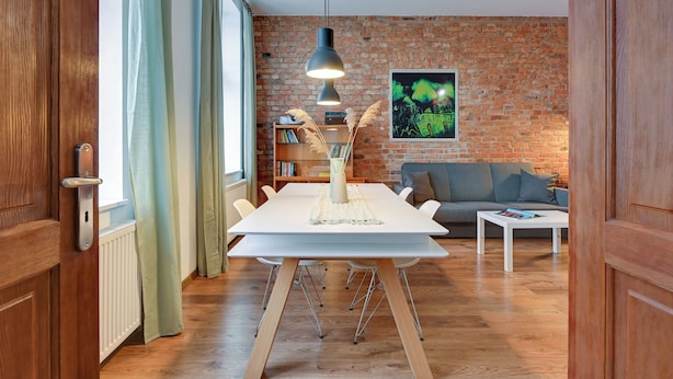 A modern living room with a white dining table, a grey sofa, and a brick wall. - City Center Art House by Downtown Apartments (Gdansk)