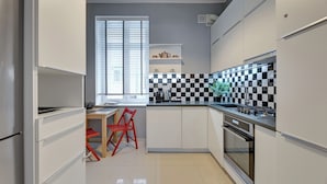 A modern kitchen with white cabinets, a checkered backsplash, a red chair, and a window with blinds. - City Center Art House by Downtown Apartments (Gdansk)