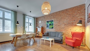 A modern living room with a brick wall, wooden flooring, a dining area with a table and chairs, a grey sofa, a red armchair, and pendant lighting. - City Center Art House by Downtown Apartments (Gdansk)