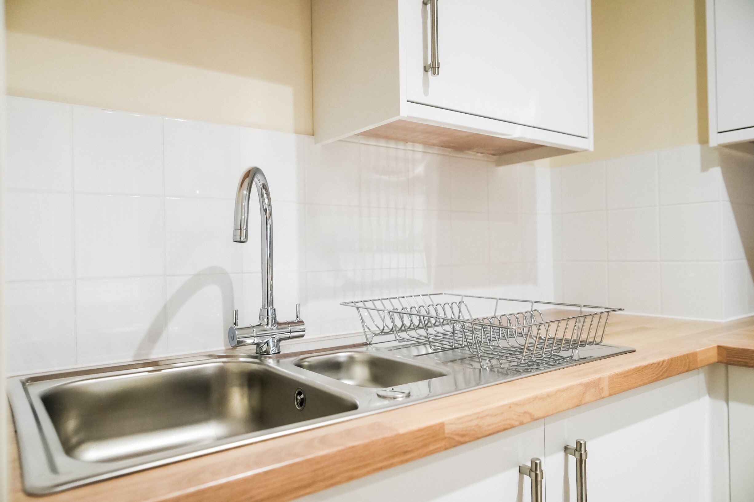 A kitchen with two stainless steel sinks, a dish rack, and white cabinets.