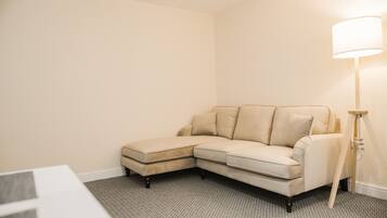 A corner living room with a beige sectional sofa, a floor lamp, and a carpeted floor.