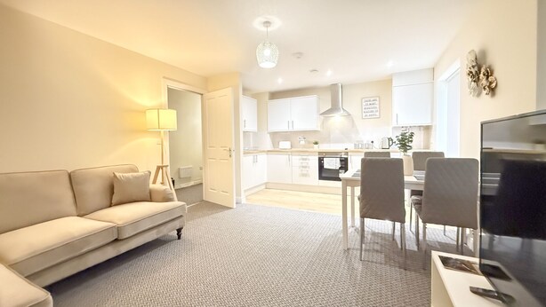 A modern living room with a sofa, a dining table with chairs, a TV, and a kitchen in the background.