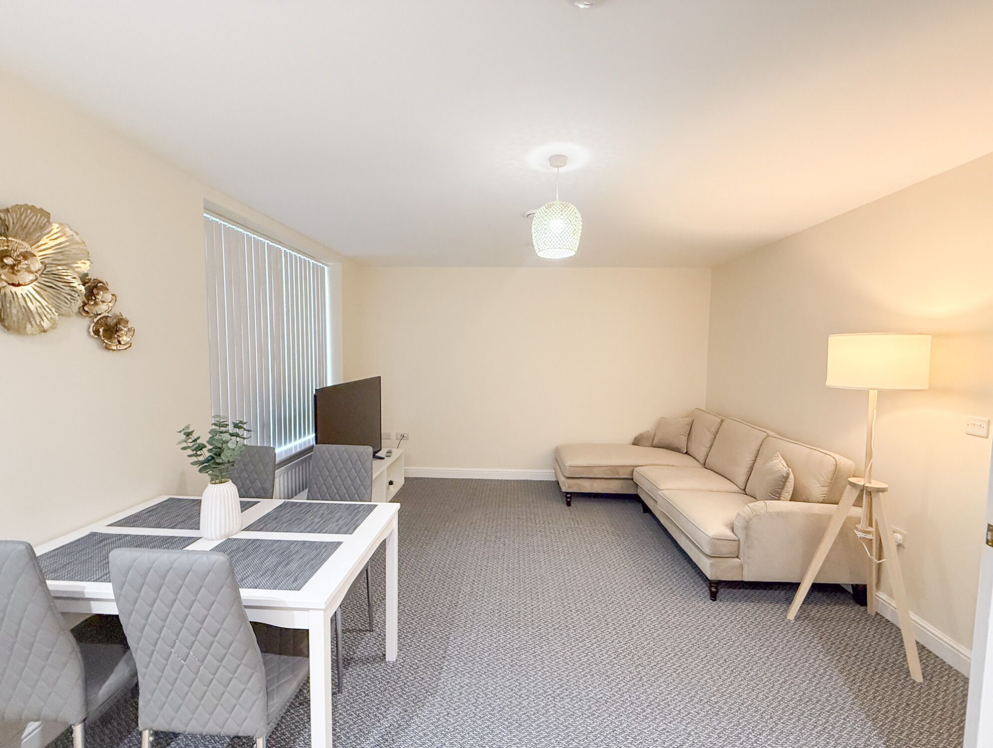A modern living room with a dining area, a beige sofa, a standing lamp, and a TV.