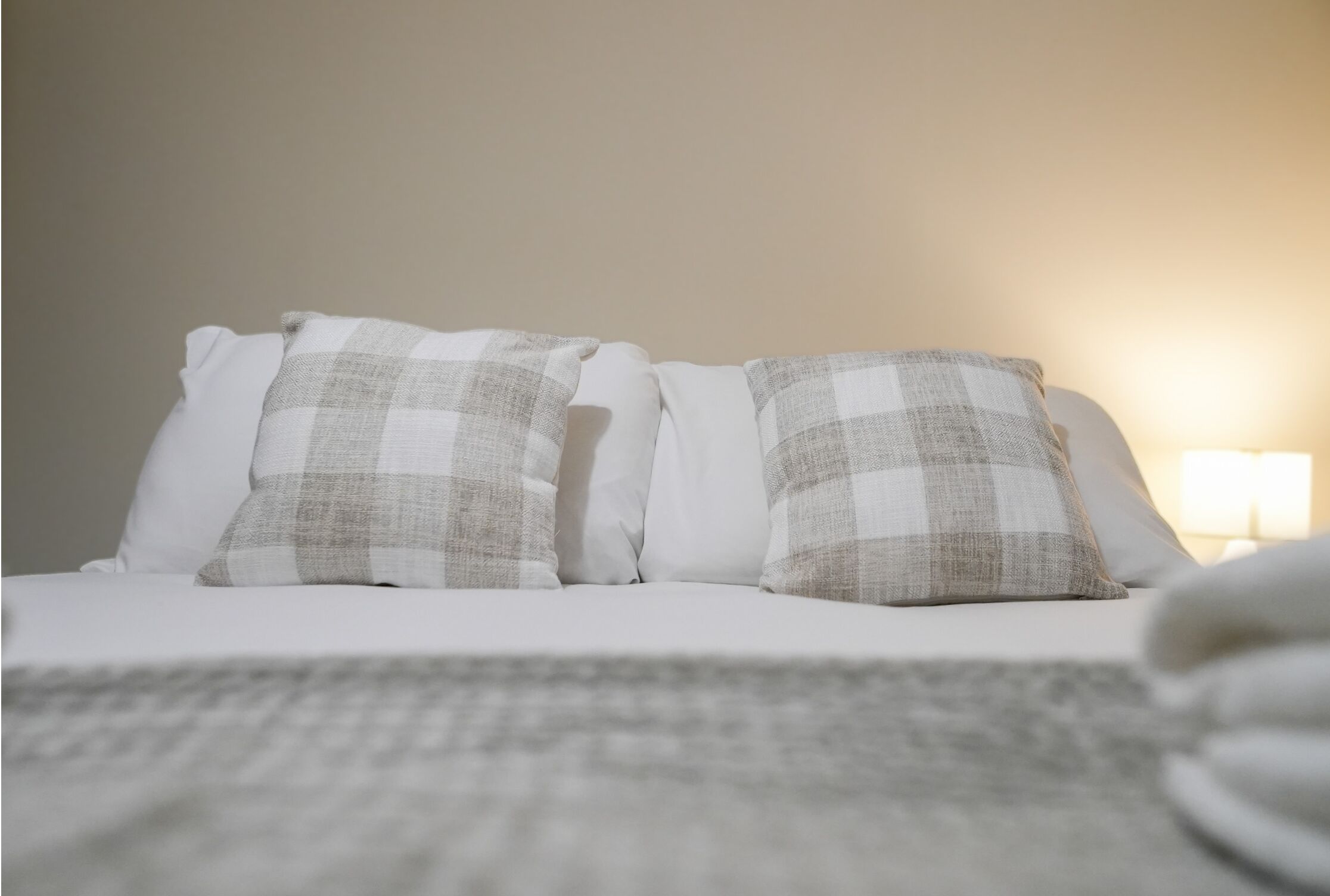 Una cama con ropa blanca y dos almohadas a cuadros.