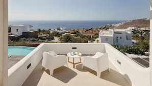 Un balcon avec des meubles blancs, une piscine et une vue sur la mer et les bâtiments.