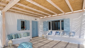 Une pièce baignée de lumière, avec un plafond en bois, des murs blancs et des volets bleus.