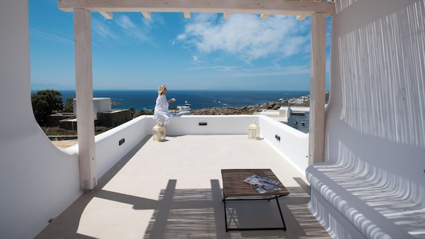 Une terrasse extérieure couverte avec vue sur la mer, une table en bois et deux lanternes.