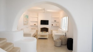 Un salon minimaliste avec des meubles blancs, une cheminée et un téléviseur à écran plat.